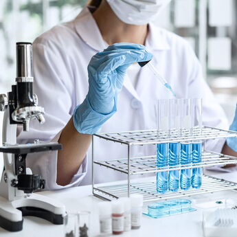 Medical in lab coat holding test tube with drop of color liquid over glass equipment working at the laboratory.